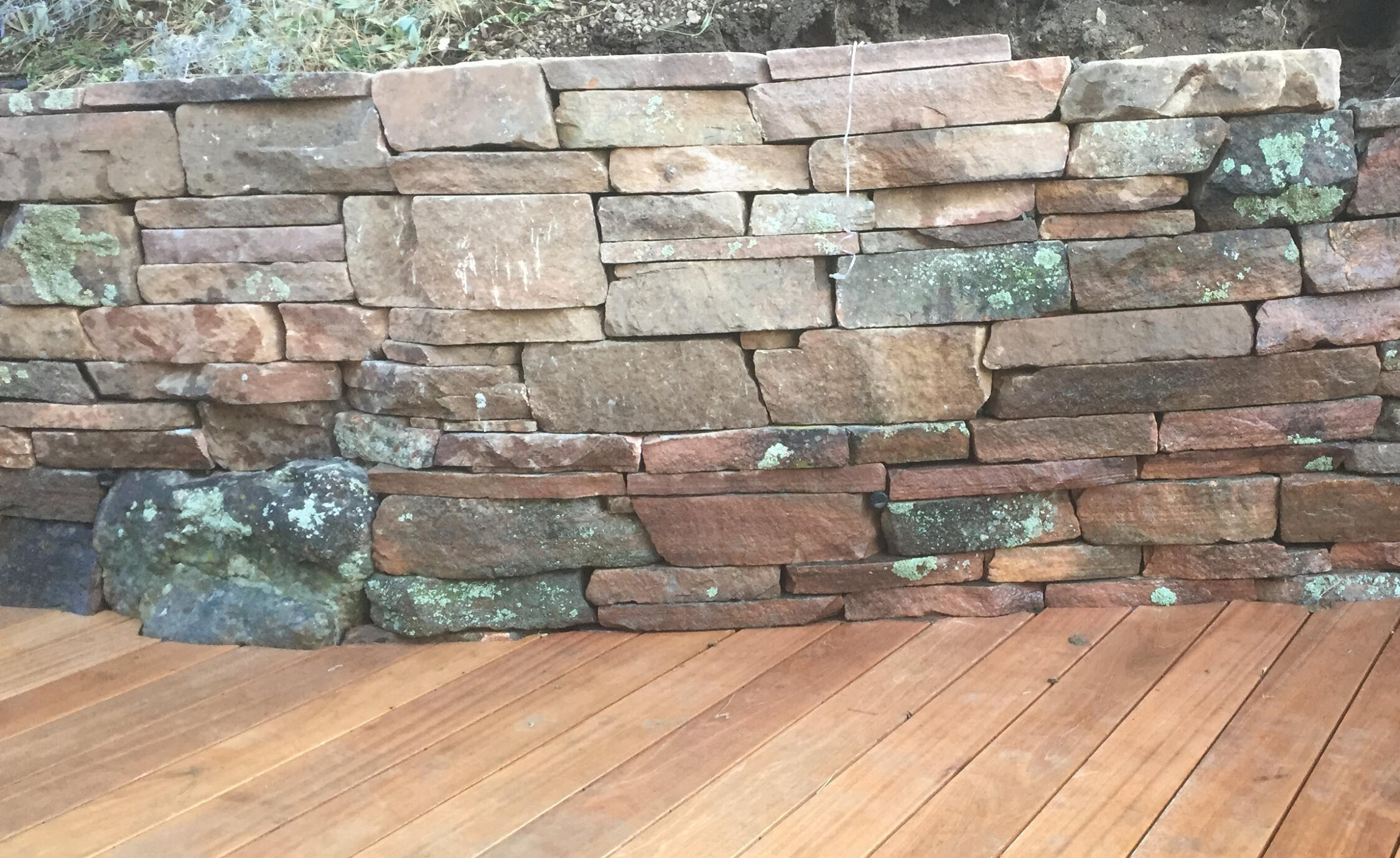 Hardwood decking cut tight to edge of moss rock stacked wall